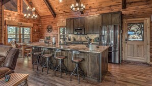 Interno rustico di una baita con una grande cucina in legno, sgabelli da bar e una zona pranzo con un divano in pelle.