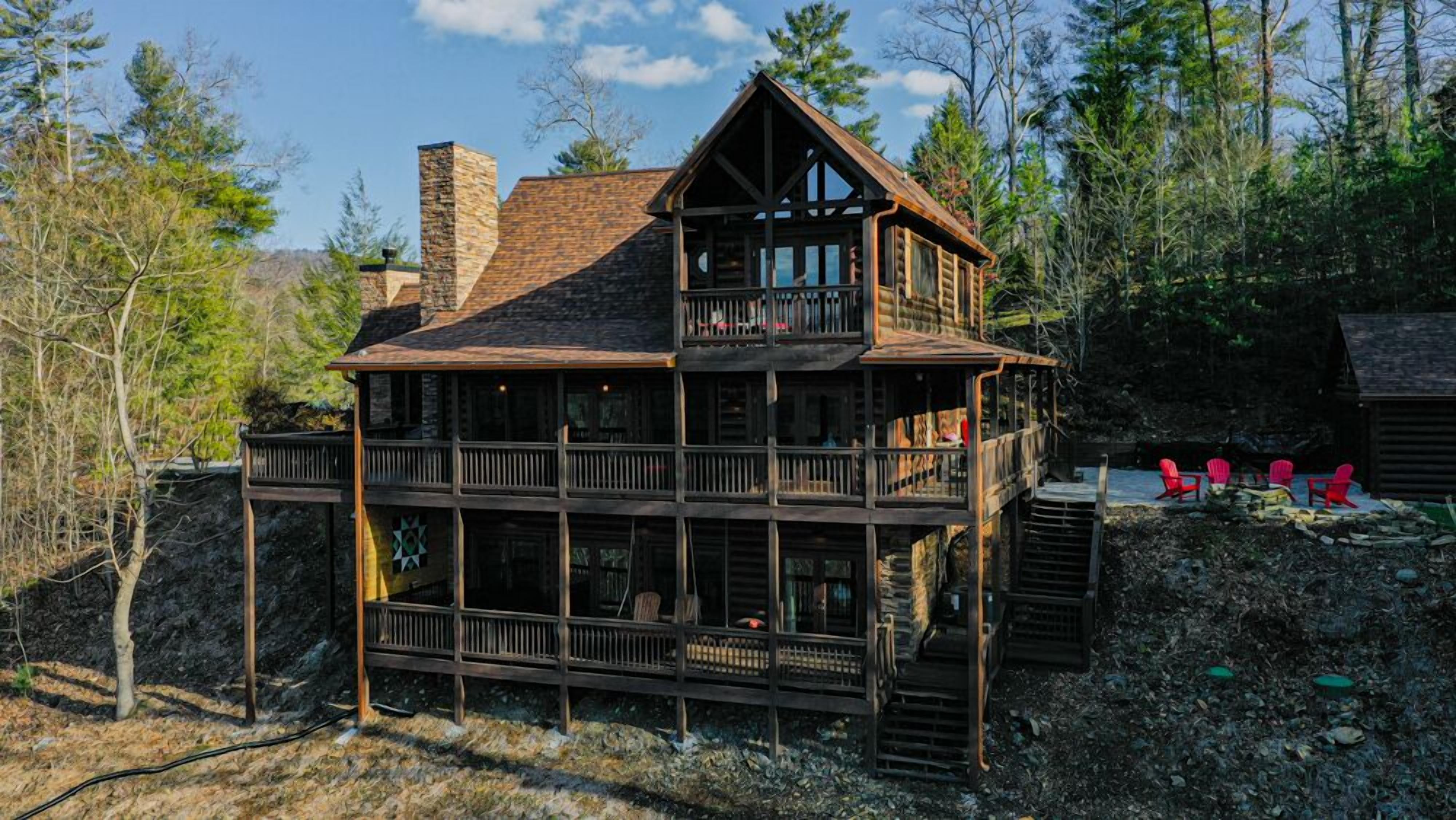 Une cabane en rondins à plusieurs étages, dotée d’un balcon et entourée d’arbres.
