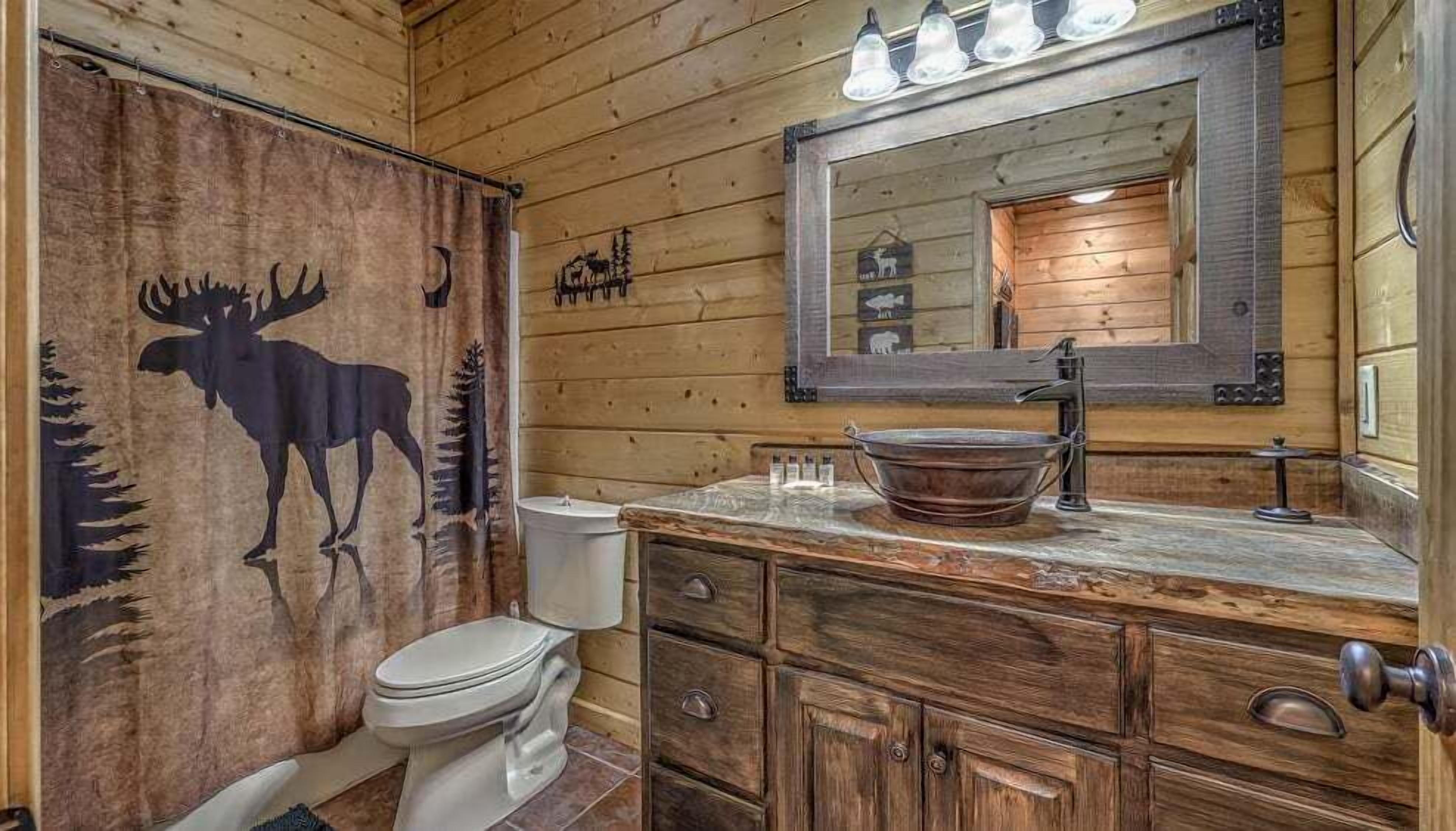 A rustic bathroom with a moose mural, a wooden vanity, a large mirror, and a modern sink.