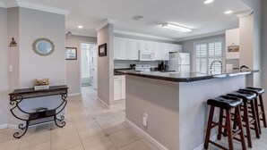 A modern kitchen with white cabinets, a central island with bar stools, and a decorative mirror on the wall.