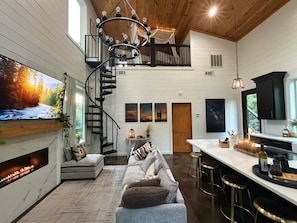 A modern interior with a spiral staircase, a large flat-screen TV, a sofa, and a bar area.