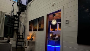 Una habitación con una escalera, una cama con iluminación LED azul, una pared con obras de arte enmarcadas y un ventilador de techo.