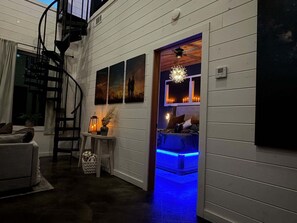 A room with a staircase, a bed with blue LED lighting, a wall with framed artwork, and a ceiling fan.