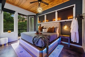 A bedroom with a large bed, bedside tables, a ceiling fan, and a view of the outdoors.