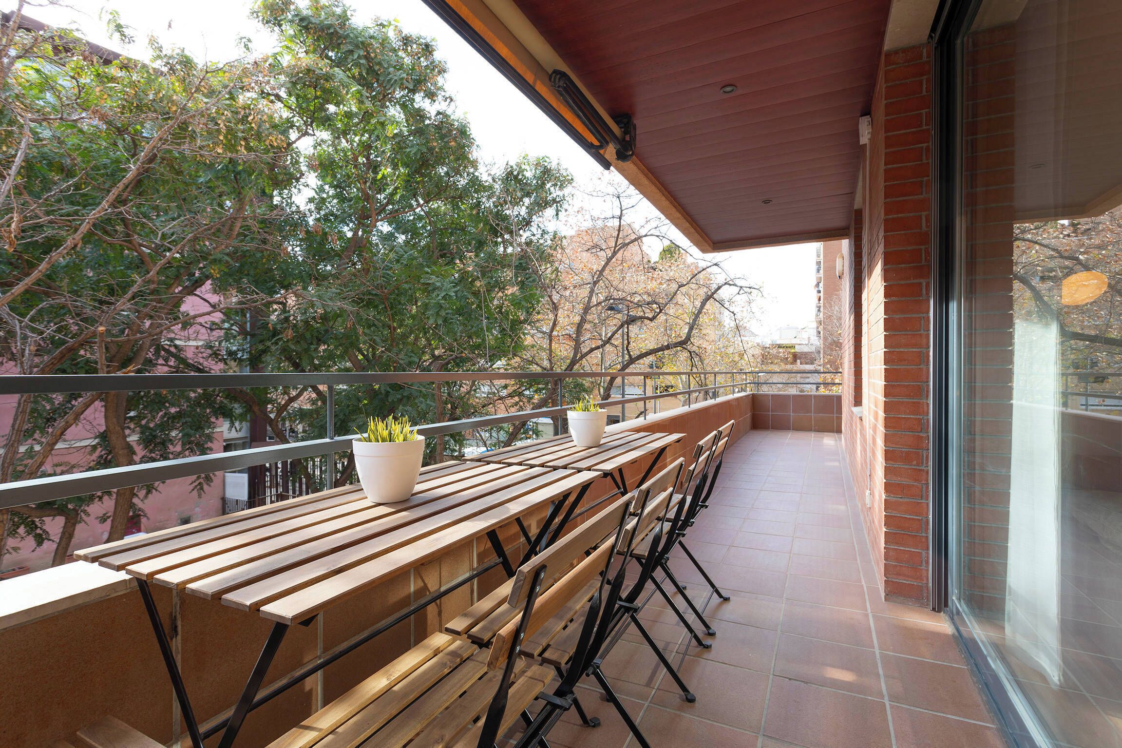 A balcony with wooden benches, potted plants, and a view of trees and buildings.