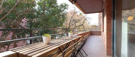 A balcony with wooden benches, potted plants, and a view of trees and buildings.