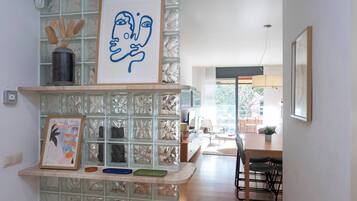 Een moderne keuken met een glazen scheidingswand, kunstwerken in lijsten, en een eethoek met een tafel en stoelen.