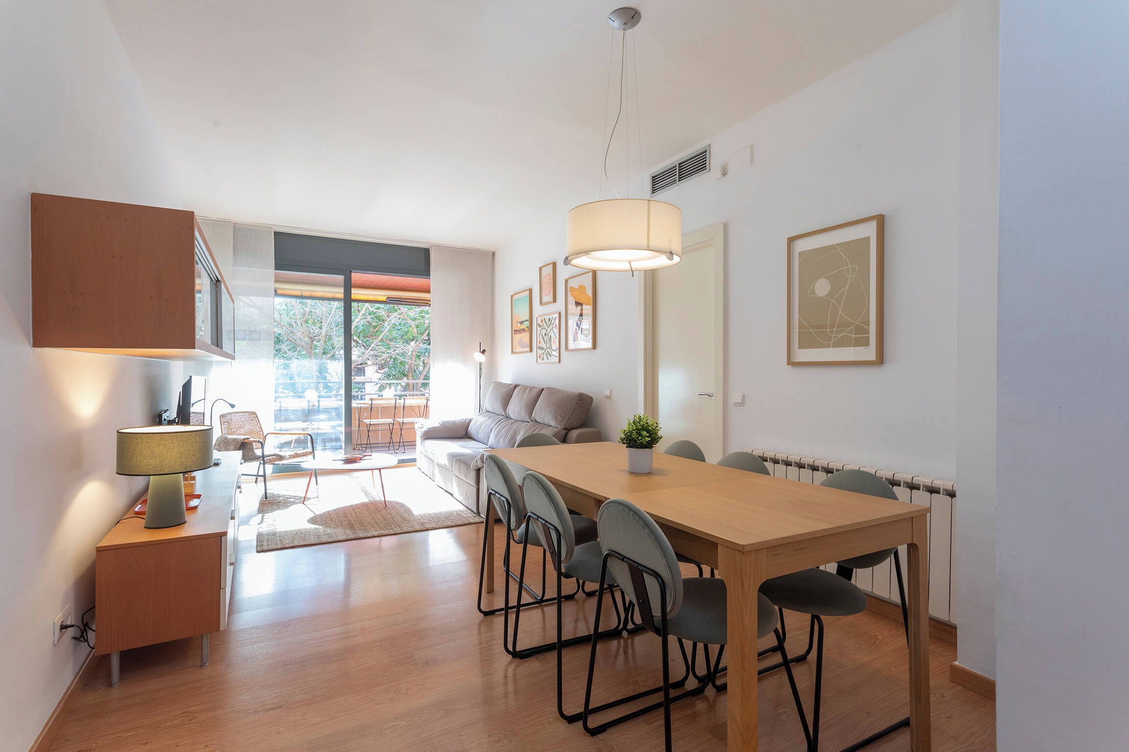 Een moderne keuken met houten kastjes, een eettafel met stoelen, een bank en een groot raam.
