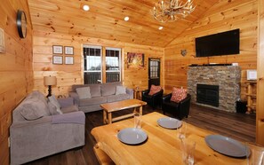 A cozy cabin interior with a wooden interior, a sofa set, a dining table with plates, and a fireplace.