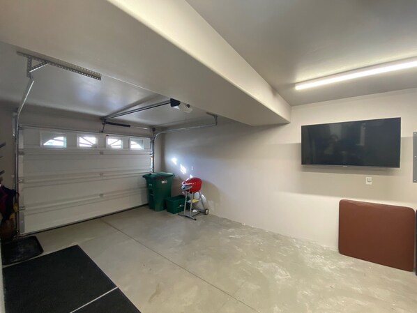 A garage with a white door, a green trash bin, a red helmet, and a mounted TV on the wall. - Ouray, CO Closest Townhome to Hot Springs Pool, Park, Trails (Ouray)