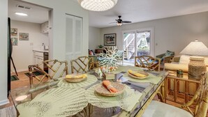 Uma sala de jantar com mesa de vidro, cadeiras de vime e um ventilador de teto.