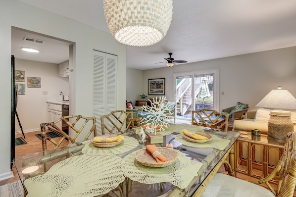 A dining area with a glass table, wicker chairs, and a ceiling fan.