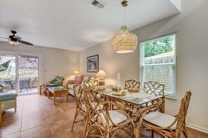 A dining area with a glass table, wicker chairs, and a hanging light fixture.