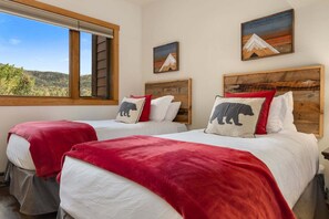 A room with two beds, each with a wooden headboard, red bedding, and a view of a mountainous landscape through a window. - Steps to Gondolas + Hot Tub & Heated Pool - 4BR/3BA - EZCancel (Steamboat Springs)