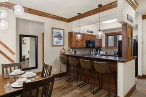 A modern kitchen with wooden cabinets, a central island with bar stools, and pendant lighting. - Steps to Gondolas + Hot Tub & Heated Pool - 4BR/3BA - EZCancel (Steamboat Springs)