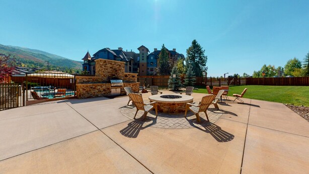 Eine Terrasse mit Feuerstelle und Gartenmöbeln, einem Stein-Barbecue und einem Pool im Hintergrund.