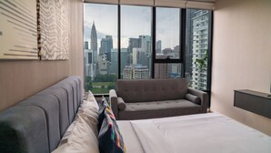 A modern hotel room with a large window offering a city skyline view, a bed, a sofa, and a small table. - Ceylonz Suites KLCC by Mana-Mana  (Kuala Lumpur)