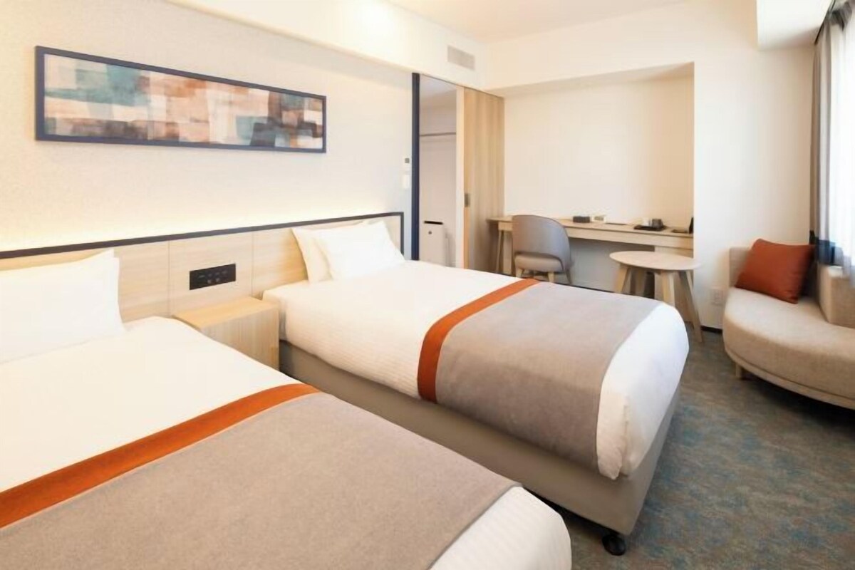 A hotel room with two beds, a desk, a chair, and a sofa.