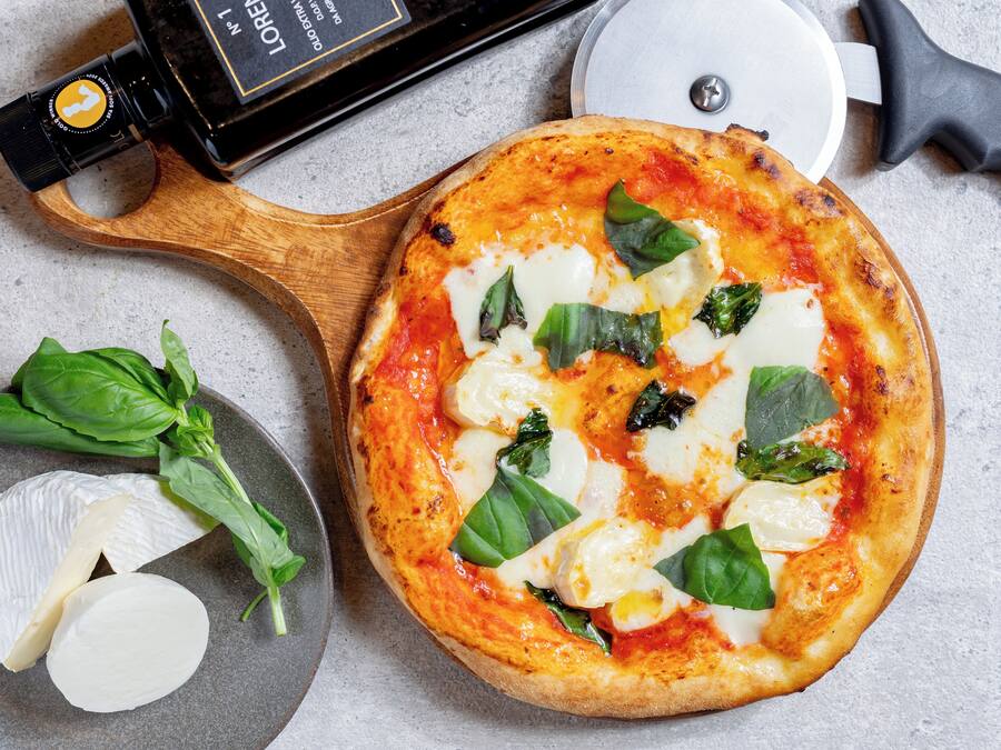 Juustolla ja basilikanlehdillä päällystetty pizza, joka on tarjoiltu puulevylle.