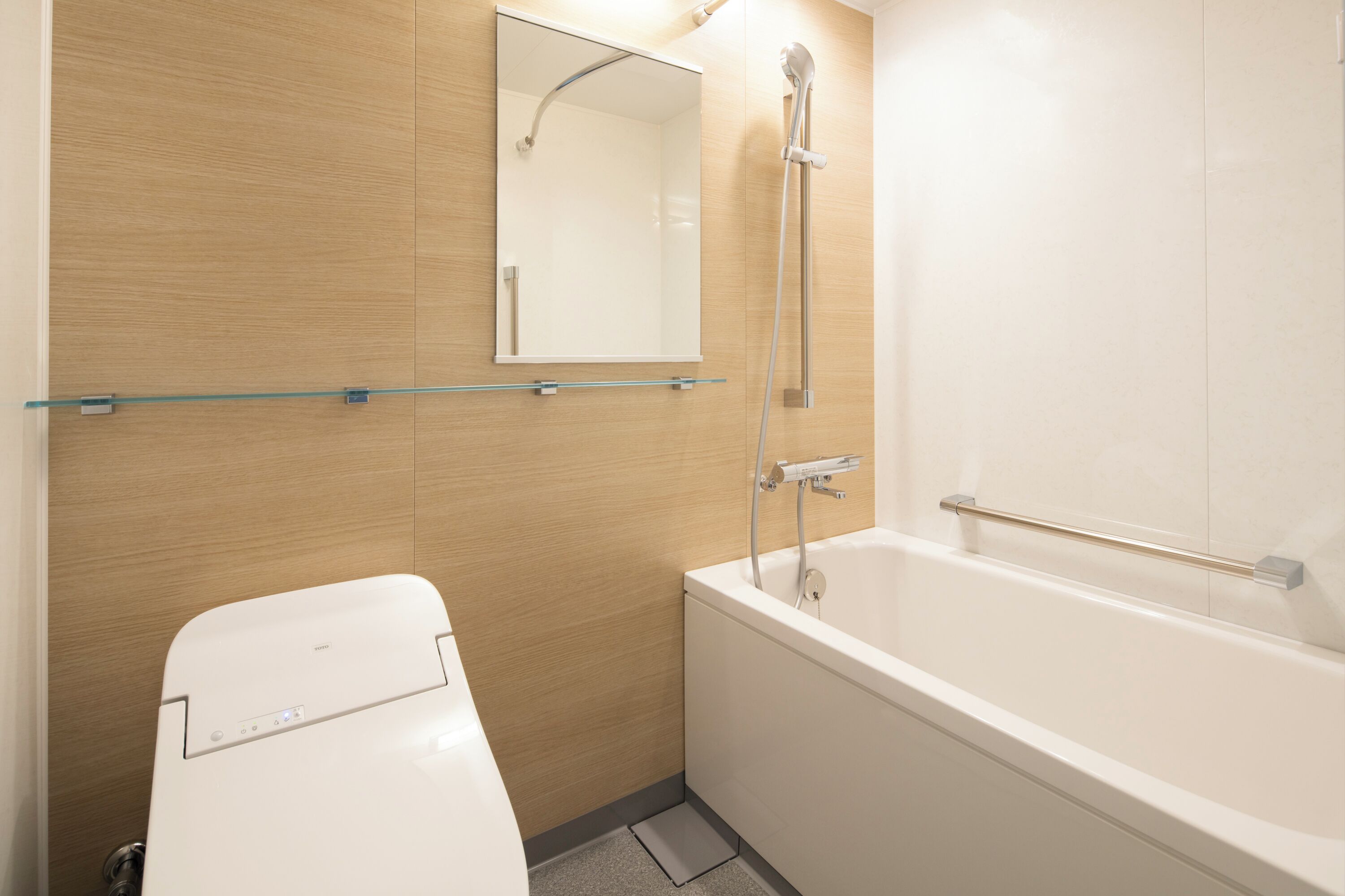 Un baño moderno con inodoro, repisa de vidrio, espejo y bañera.
