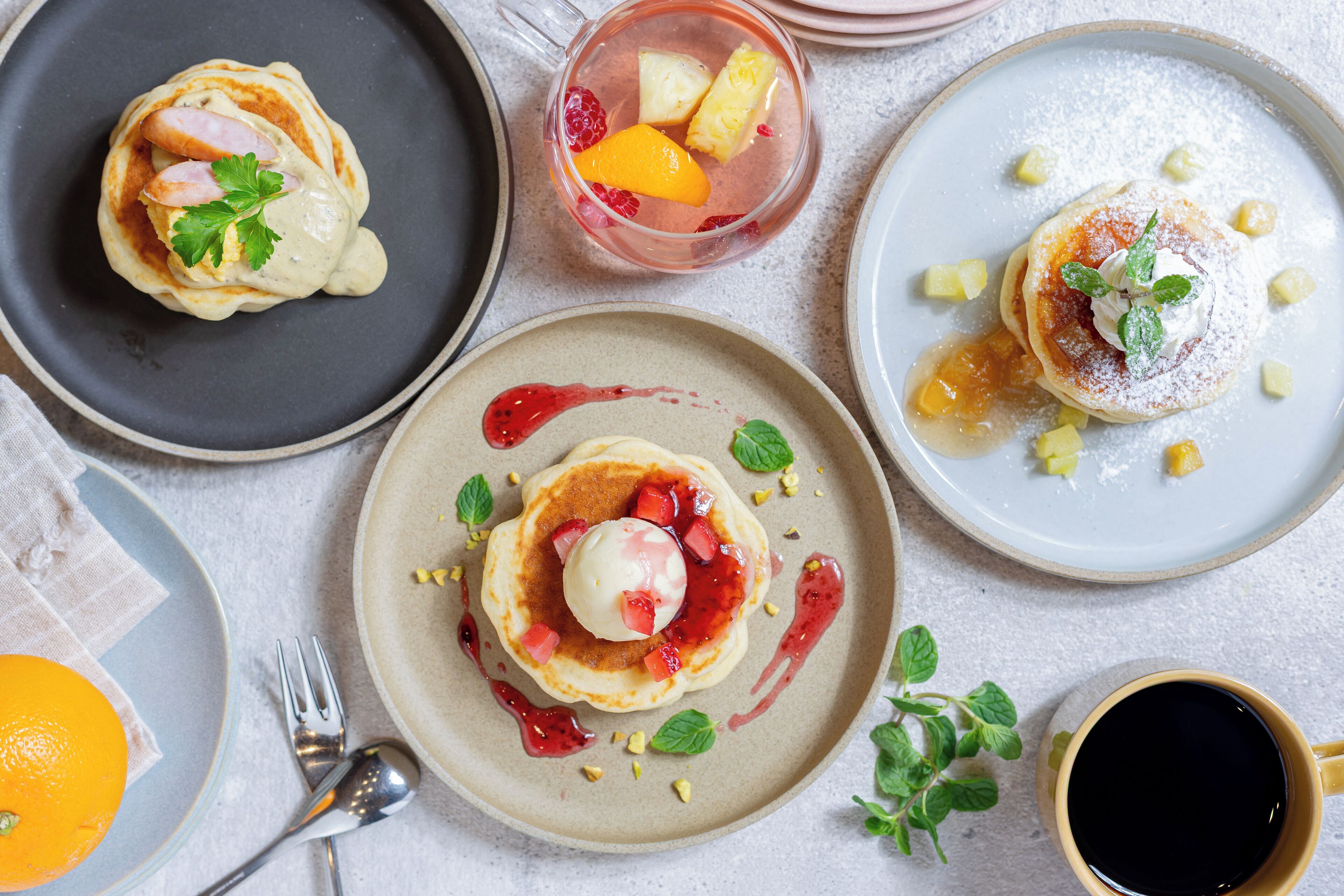 Variedad de platos para el desayuno, incluyendo panqueques con fruta y helado, un batido de frutas y una taza de café.