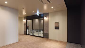 A modern hotel lobby with a wooden floor, a glass door entrance, and a wall-mounted information board.