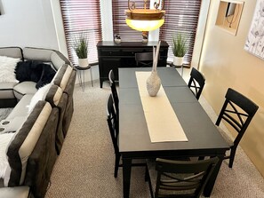 Uma área de refeições com mesa, cadeiras, um sofá e plantas em vasos.