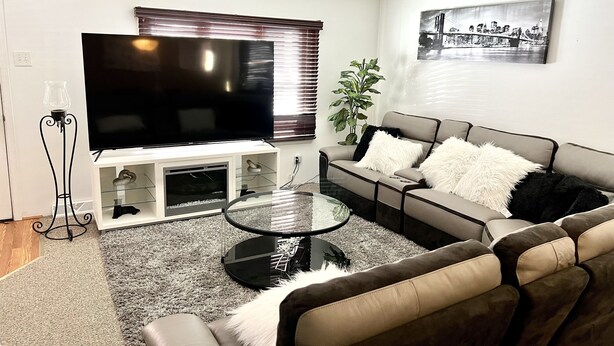 A modern living room with a flat-screen TV, a sofa, a glass coffee table, and a potted plant. - Welcome to the Fort. Walking Distance to Niagara Falls. (Niagara Falls)
