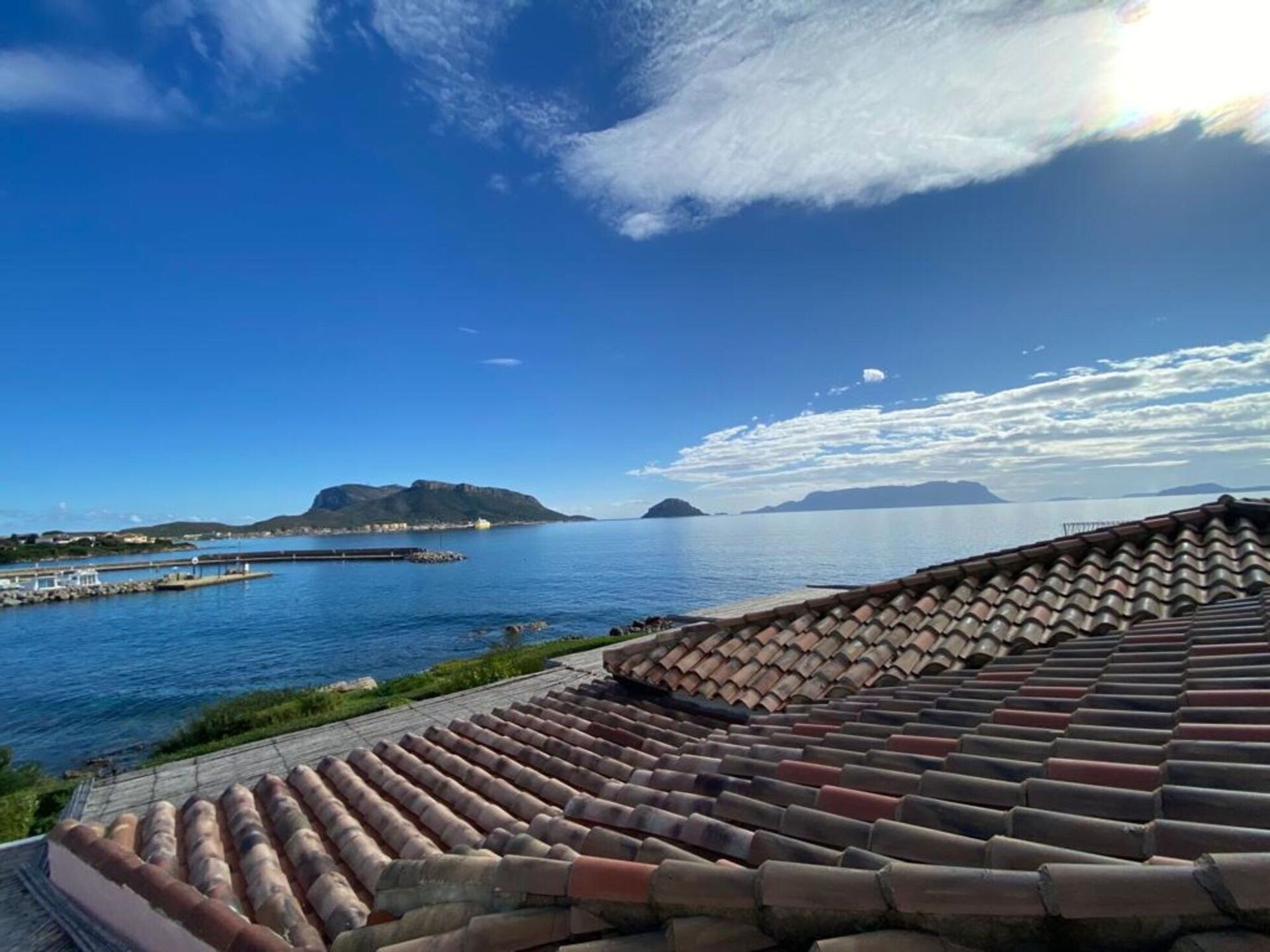 Vista costanera amb cel serè, una massa d'aigua i una construcció amb teules de color terracota.