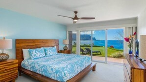 A bedroom with a wooden bed, a ceiling fan, and a view of the ocean through large sliding glass doors.