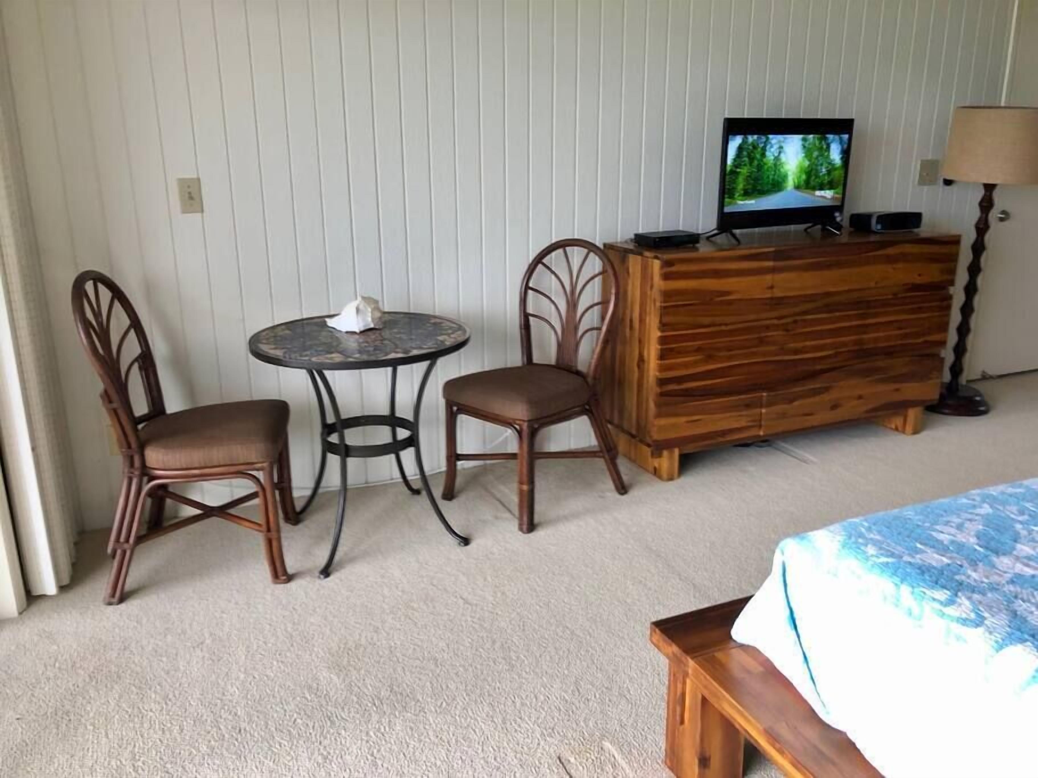 Ein Hotelzimmer mit einem Bett, einer Holzkommode, einem Fernseher, zwei Stühlen und einem kleinen runden Tisch.