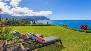 A grassy area with two lounge chairs and a pool in the background.