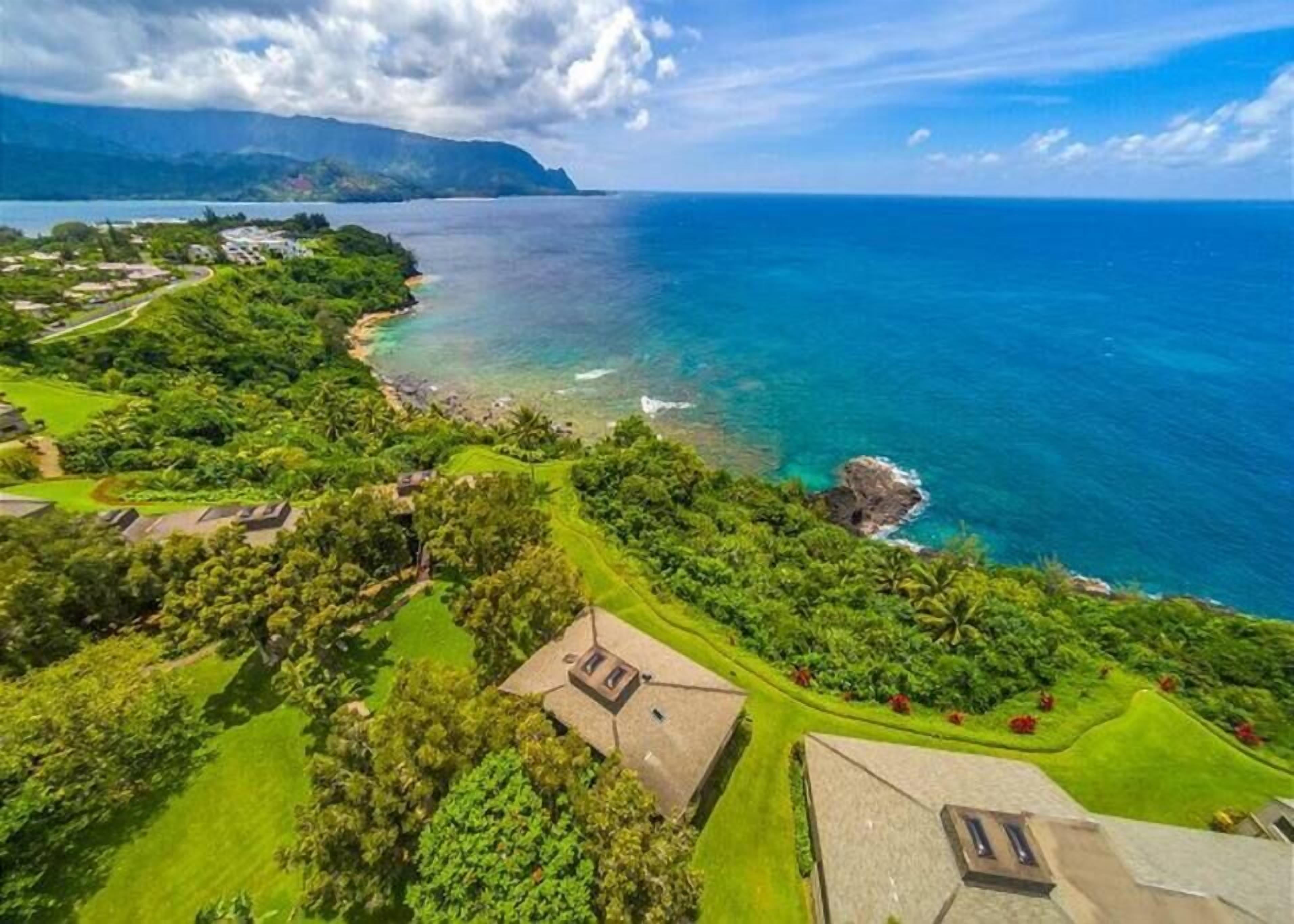 A coastal property with lush greenery, a beach, and a view of the ocean.