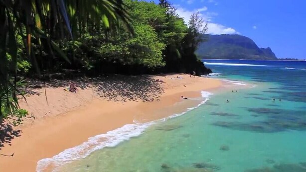 Uma praia com águas turquesa cristalinas, areal arenoso e vegetação exuberante.