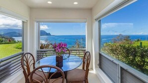 Uma área de refeições com mesa e cadeiras, um vaso de flores e vista para o oceano e montanhas.