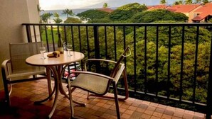 Un balcone con tavolo e sedie, affacciato su un paesaggio verdeggiante con palme e vista sull'oceano.