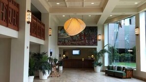 Un'ampia hall con soffitto alto, un grande lampadario, una reception e un'area lounge con vista sull'esterno.