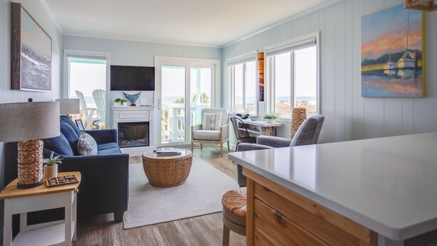 A modern living room with a fireplace, comfortable seating, and large windows offering a view of the outdoors.