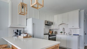 A modern kitchen with white cabinetry, a large island, and a hanging light fixture.