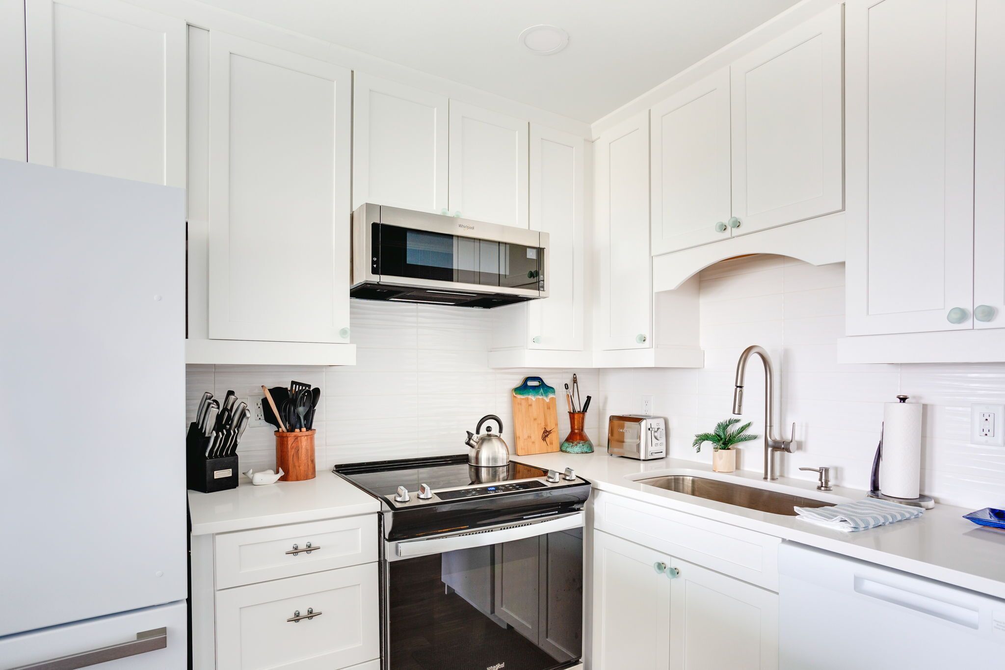 Una cocina moderna con armarios blancos, una estufa de acero inoxidable, un microondas y un fregadero.