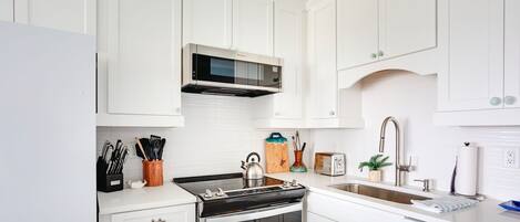 Una cocina moderna con armarios blancos, una estufa de acero inoxidable, un microondas y un fregadero.