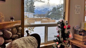 Una habitación con un amplio ventanal que muestra un paisaje montañoso nevado y un árbol de Navidad decorado con adornos.