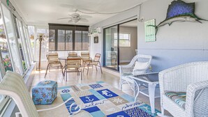 Une terrasse ensoleillée, meublée de meubles en osier, dotée d’un ventilateur de plafond et ornée d’un poisson-voile décoratif au mur.