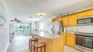 Une cuisine spacieuse avec des meubles en bois, un grand îlot central doté de tabourets, un réfrigérateur, un four et un four à micro-ondes.