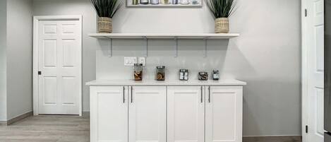 A kitchen with white cabinets, a white countertop, and two potted plants on shelves above.