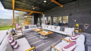 A modern outdoor living area with a sofa set, coffee table, and chairs, overlooking a scenic landscape. - Sleeps 20 , Game Barn, Pool, Hot Tub, Luxe Retreat (Dripping Springs)