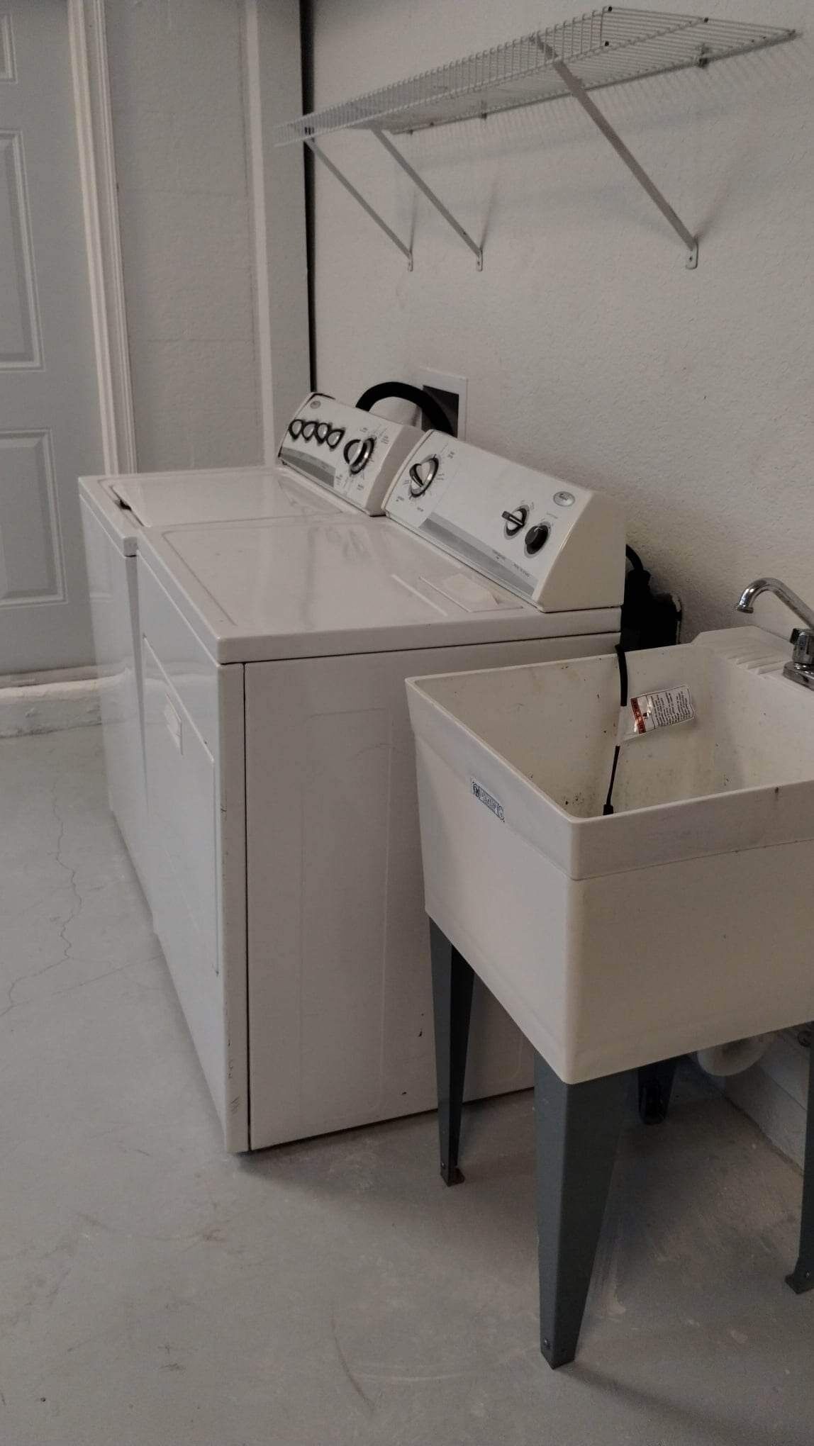 A laundry area with a front-loading washer and dryer, a sink, and a drying rack.