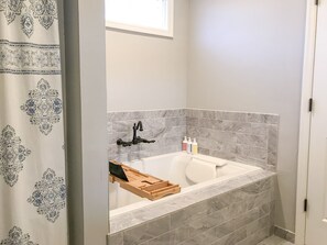 A bathroom with a bathtub, a wooden tray, and toiletries on the side. - 4 bedroom Masters Rental 5 miles from Augusta National (Martinez)