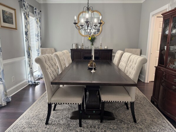 Uma sala de jantar com uma mesa de madeira escura, cadeiras estofadas, um candelabro e um aparador.