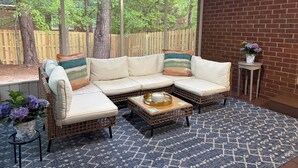A sectional sofa with cushions, a small round table with a vase, and a patterned rug in a room with large windows and a brick wall. - 4 bedroom Masters Rental 5 miles from Augusta National (Martinez)